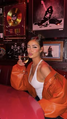 a woman sitting at a table with a glass of wine in her hand and pictures on the wall behind her