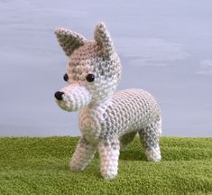 a crocheted dog standing on top of a grass covered field with blue sky in the background