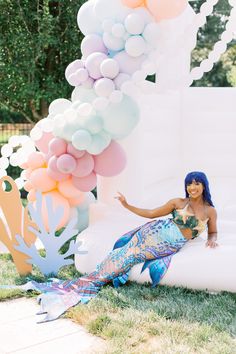 a woman sitting on top of a white couch next to balloons and mermaid tailes