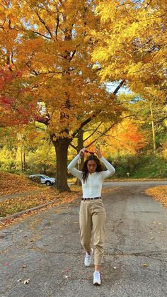 a woman in white shirt and khaki pants walking down road with trees full of leaves