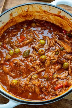 a pot filled with meat and olives on top of a wooden table