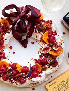 a white cake with fruit on it and a red bow tied around the top is surrounded by other desserts