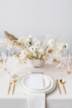 a table set with white and gold place settings, silverware and flowers in a vase