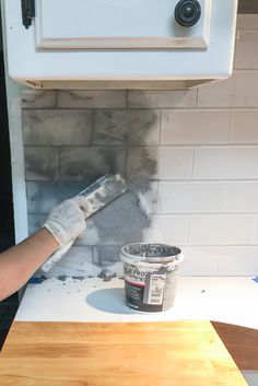 a person with gloves on painting a wall in a room that has white tiles and gray grout