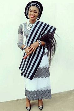 a woman wearing a black and white dress with a large scarf on her head, standing in front of a wall