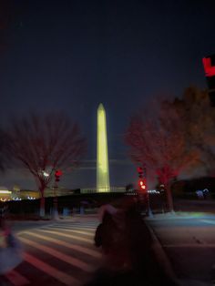 the washington monument is lit up at night with red traffic lights and trees in the foreground