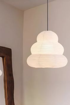 a white lamp hanging from the ceiling next to a mirror and wooden framed object in a room