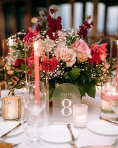 a centerpiece with candles and flowers is displayed on a table in front of other place settings