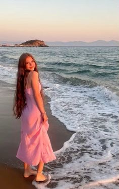 a woman standing on top of a sandy beach next to the ocean with waves coming in