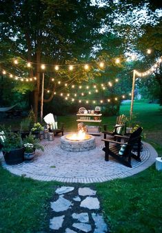 a fire pit surrounded by chairs and lights in the middle of a yard with lots of greenery