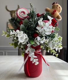 a red mason jar filled with flowers and candy canes on top of a table