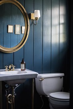 a white toilet sitting next to a bathroom sink under a round mirror in a blue room