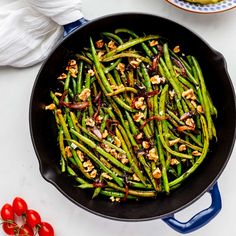 green beans with walnuts in a skillet on a white countertop next to tomatoes