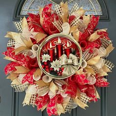 a red and gold christmas wreath hanging on a front door with two candles in the center