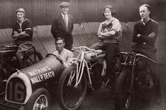 a group of men standing next to each other in front of an old fashioned car