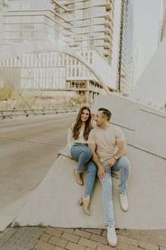 a man and woman sitting next to each other on top of a cement wall in front of tall buildings