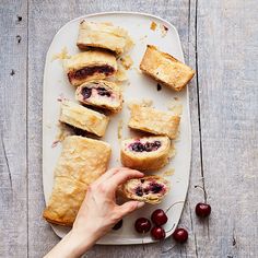 a person holding a piece of food on top of a white plate next to some cherries