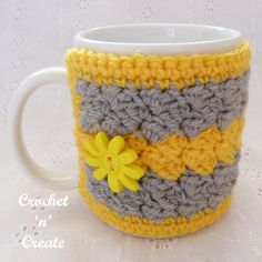 a crocheted coffee cup with a yellow flower on the side and gray stripes