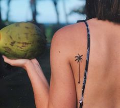 a woman with a palm tree tattoo on her back holding a green watermelon