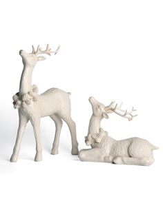 two white deer figurines sitting next to each other on a white surface with one laying down