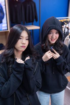 two young women standing next to each other looking at their cell phones in a clothing store