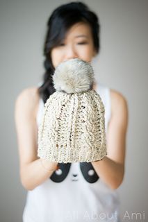 a woman holding up a knitted hat with a pom - pom in front of her face