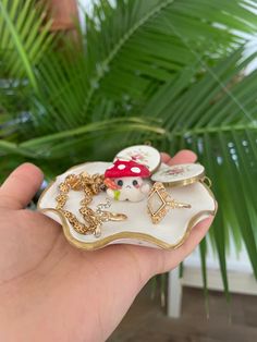 a hand holding a small white and gold plate with charms on it's side