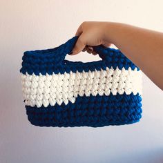 a hand holding a crocheted blue and white purse with two stripes on it