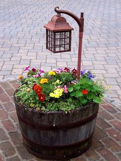 a wooden barrel with flowers in it on the ground next to a street light and lamp post