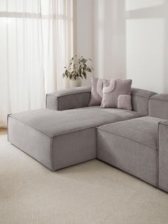 a large gray couch sitting on top of a white carpeted floor next to a window