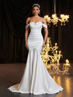 a woman in a white wedding dress standing next to a chandelier with candles