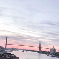 boats on the water in front of a bridge with a sky line behind it at sunset