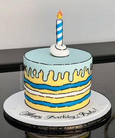 a blue and yellow birthday cake with a single lit candle on it's top