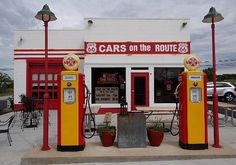 an old gas station with cars on the route 66 sign and two red yellow and white pumps