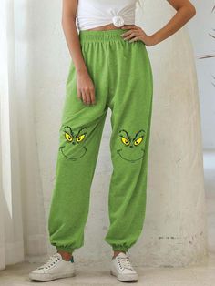 a woman standing in front of a white wall wearing green sweatpants with yellow eyes