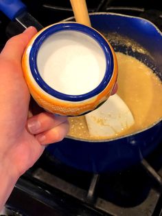 a person holding a spoon over a pan filled with liquid and cheese on the stove