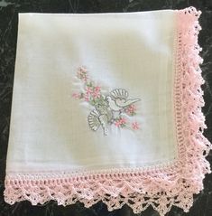 a white handkerchief with pink flowers and a bird embroidered on the front, sitting on a marble surface