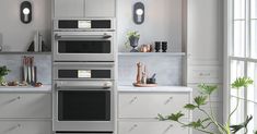 a modern kitchen with stainless steel appliances and white counter tops, along with potted plants