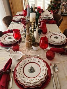 the table is set for christmas dinner with red and white plates, silverware, and candlesticks