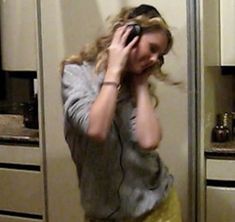 a woman standing in front of a kitchen holding a cell phone to her ear and talking on the phone