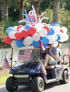 a man driving a golf cart with balloons on the back and an american flag decoration above it