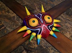 a colorful mask with spikes on it sitting on top of a wooden cross in the middle of a floor