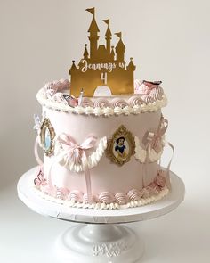 a pink cake decorated with princess castle and nameplates on top, sitting on a white pedestal