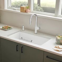 a white kitchen sink sitting under a window next to a bowl of salad on top of a counter