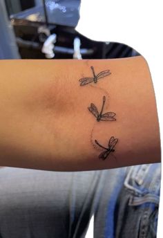 a woman's arm with three small dragonflies on the back of her arm