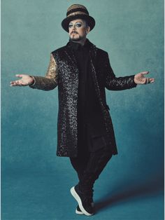 a man in a black suit and hat with his hands out while standing on a blue background