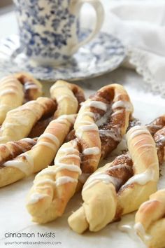 cinnamon twists with icing sitting on a table next to a cup and saucer