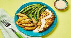 a blue plate topped with chicken, green beans and potatoes next to a bowl of ranch dressing