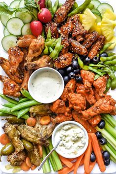 a white plate topped with chicken wings and veggies next to dips on top of cucumbers