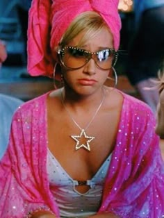 a woman wearing sunglasses and a star necklace in front of other people sitting at a table